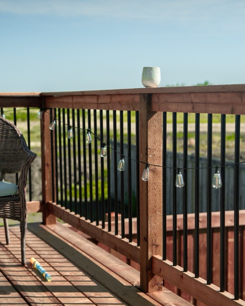 Deck railing strung with patio lights above cedar decking